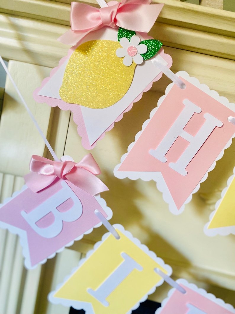 May include: A pink and yellow banner with the words "Happy Birthday" in white letters. The banner is decorated with pink bows, a lemon slice, and green leaves.