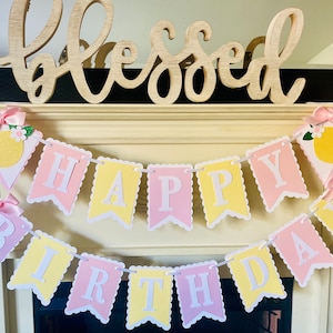 May include: A pink and yellow banner with the words "Happy Birthday" decorated with lemons and bows.