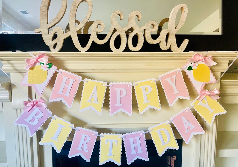 May include: A pink and yellow banner with the words "Happy Birthday" decorated with lemons and bows.
