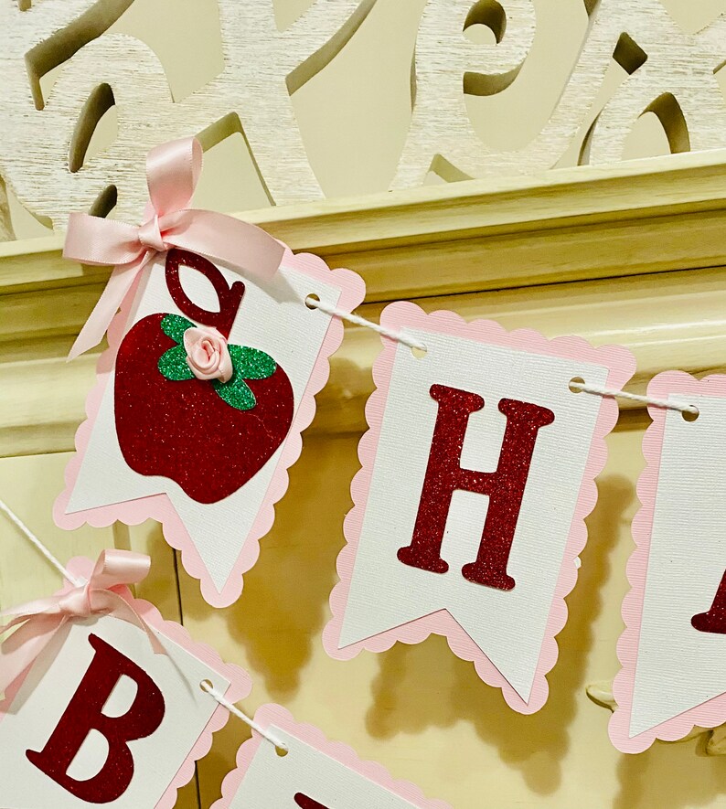 May include: A red glitter apple with a pink bow and a green leaf, a white banner with pink scalloped edges and red glitter letters spelling "Happy"