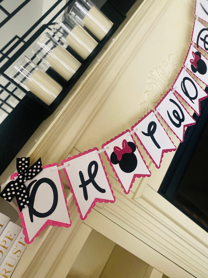 May include: Pink and black Minnie Mouse themed banner with the words "One" and "Party" in black script. The banner is made of glitter cardstock and has a scalloped edge.