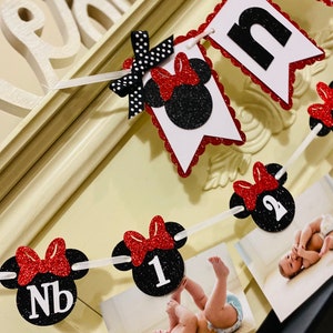 May include: A red and black Minnie Mouse themed banner with the word "one" and numbers 1 and 2. The banner is decorated with red bows and black polka dots. There are photos of a baby in the banner.