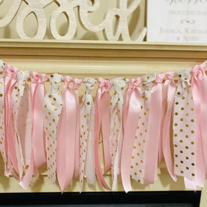 May include: A pink and gold polka dot ribbon garland. The garland features alternating ribbons of solid pink, white with gold polka dots, and white with a scalloped edge. The garland is hanging in front of a fireplace.