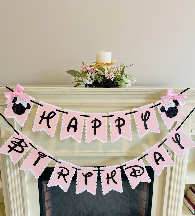 May include: Pink and black Happy Birthday banner with Minnie Mouse ears on each end. The banner is strung on a black string and has a scalloped edge.