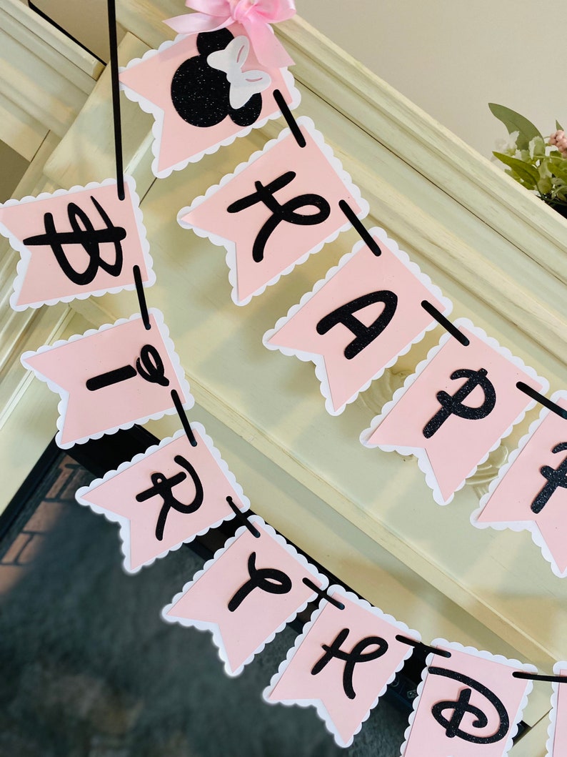 Puede incluir: Bandera de Feliz Cumplea&ntilde;os rosa y negra con una cabeza de Mickey Mouse negra al final. La bandera tiene bordes festoneados y letras negras.