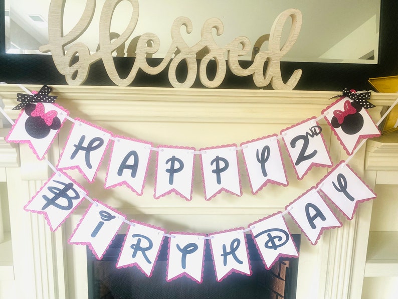 May include: A pink and white banner with black lettering that reads "Happy 2nd Birthday". The banner is decorated with two black and pink Minnie Mouse heads.