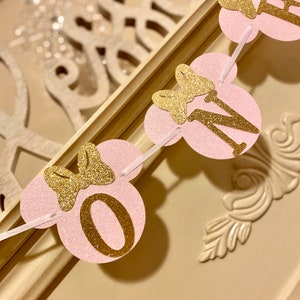 Op de afbeelding: Roze en gouden glitterbanner met het woord "EEN" in gouden letters en een gouden strik op elke letter. De banner is perfect voor een eerste verjaardagsparty.