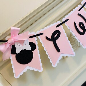 May include: Pink and black banner with scalloped edges. The banner says "Welcome" and features a black and white Minnie Mouse head with a pink bow.