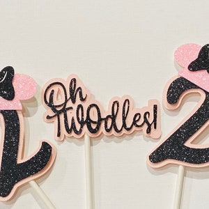 May include: Three pink and black glitter cake toppers with a black bow and ears. The toppers say "Oh Twodles!" and "2".