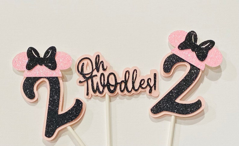 May include: Three pink and black glitter cake toppers with a black bow and ears. The toppers say "Oh Twodles!" and "2".