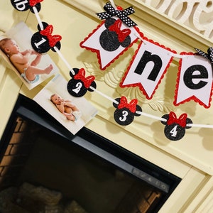 May include: A red and black Minnie Mouse themed first birthday banner with photos of a baby. The banner has red bows, black polka dots, and white numbers 1 through 4. The banner says "one" in black letters.