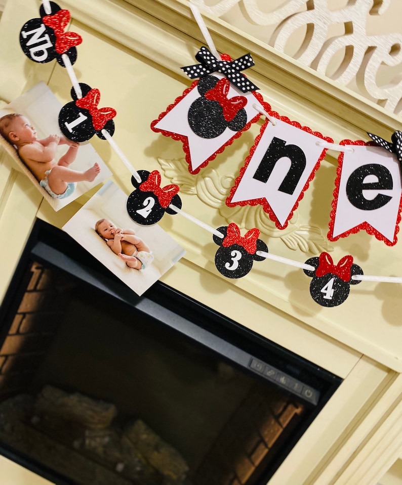 May include: A red and black Minnie Mouse themed first birthday banner with photos of a baby. The banner has red bows, black polka dots, and white numbers 1 through 4. The banner says "one" in black letters.
