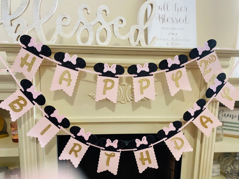May include: Pink and black Happy 2nd Birthday banner with Minnie Mouse ears. The banner is made of glitter cardstock and has gold letters.