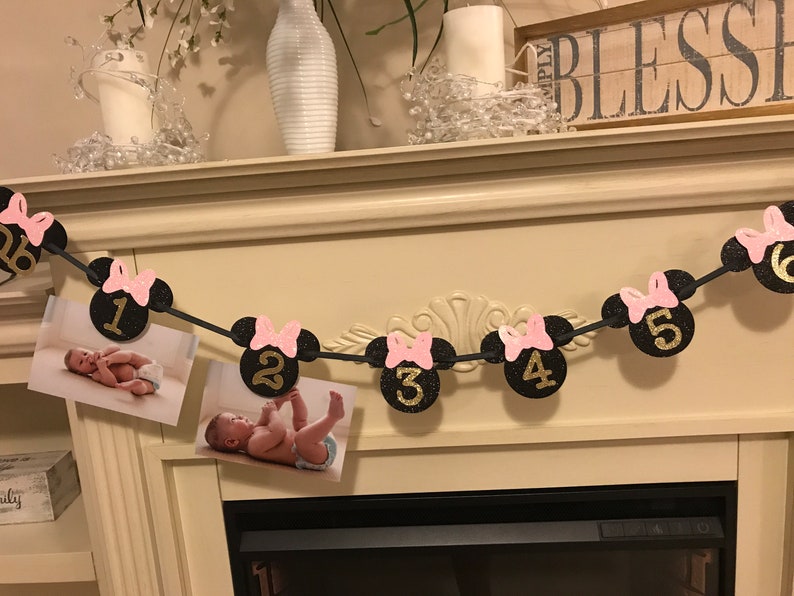 May include: A black and pink Minnie Mouse-themed monthly photo banner. Each circle features a number from 1 to 6 in gold glitter, with a pink bow. Photos of a baby are attached to the banner.