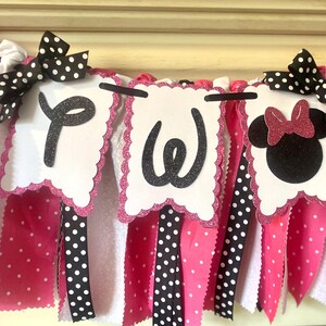May include: A festive banner with white, pink, and black polka dot ribbons and bows. The banner features three white scalloped-edge pennants with black glitter letters and a Minnie Mouse silhouette, perfect for a birthday party.