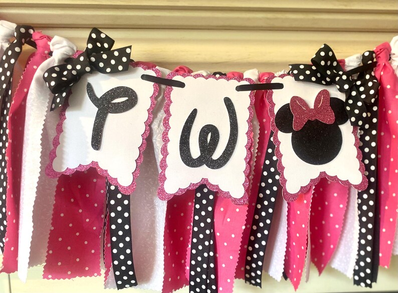 May include: A festive banner with white, pink, and black polka dot ribbons and bows. The banner features three white scalloped-edge pennants with black glitter letters and a Minnie Mouse silhouette, perfect for a birthday party.