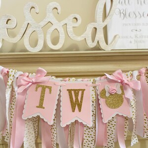 May include: Pink and gold banner with the letters "TW" and a Minnie Mouse silhouette. The banner has pink and white ribbons with gold polka dots and is decorated with pink bows. The word "Blessed" is in the background.