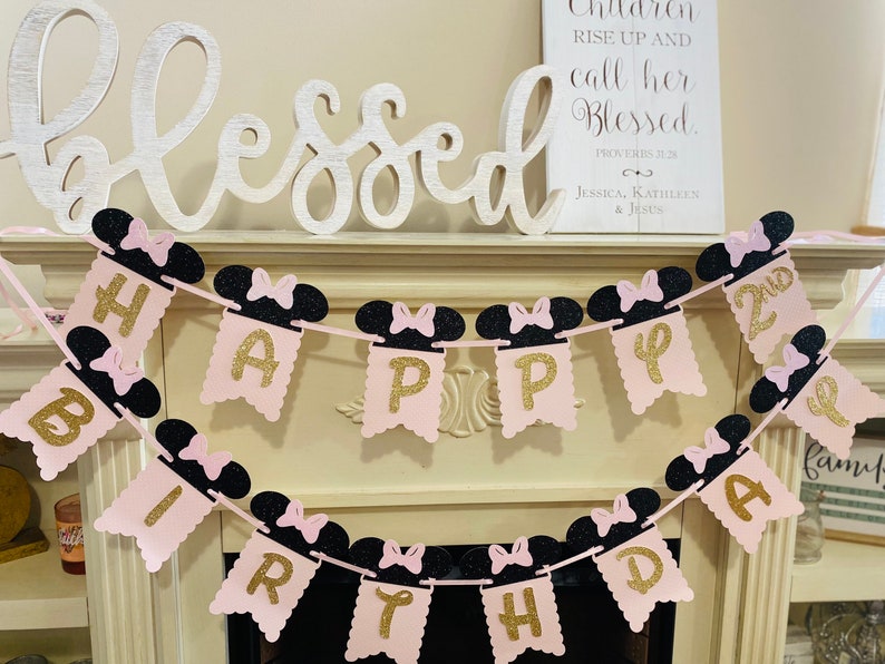 May include: Pink and black birthday banner with gold glitter letters spelling "Happy Birthday" and "2nd". The banner features Minnie Mouse ears with black bows.