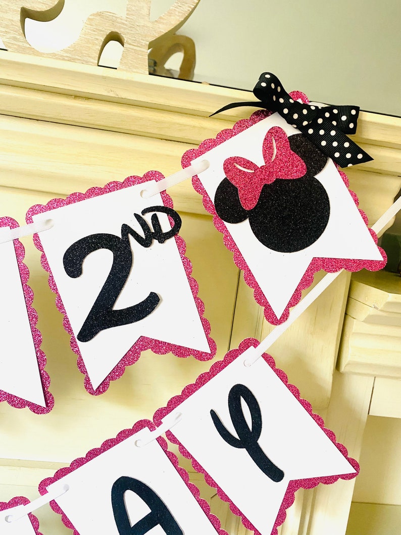 May include: Pink and black glitter banner with the words "2nd" and "Birthday" in black letters. The banner also features a black and pink Minnie Mouse head with a pink bow.