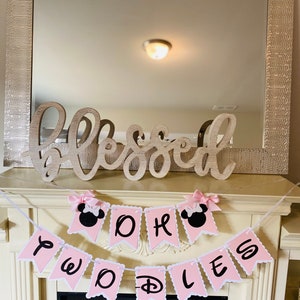 May include: Pink and black banner with the words "Oh Boy Two Doodles" and Mickey Mouse ears on each end. The banner is hanging above a fireplace with a wooden sign that says "Blessed" above it.
