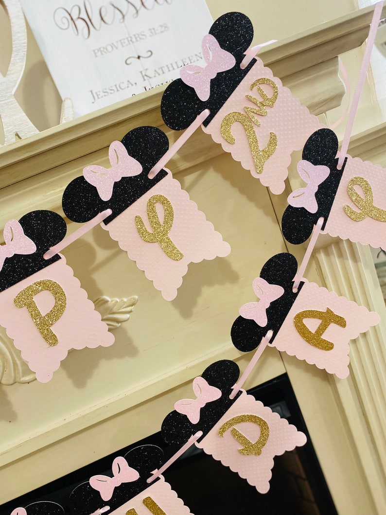 May include: Pink and black banner with gold glitter letters spelling "Happy 2nd Birthday". Each letter is on a pink scalloped flag with a black Minnie Mouse head with a pink bow on top.