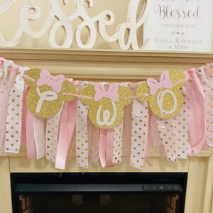May include: A decorative banner with gold glitter mouse head cutouts spelling "OWE" with pink bows. The banner is adorned with pink and white polka dot ribbons and tulle, creating a festive and celebratory look.