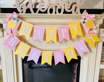 May include: A yellow and pink banner with the words "Happy Birthday" in white letters. The banner is decorated with lemons and bows.