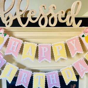 May include: A yellow and pink banner with the words "Happy Birthday" in white letters. The banner is decorated with lemons and flowers.