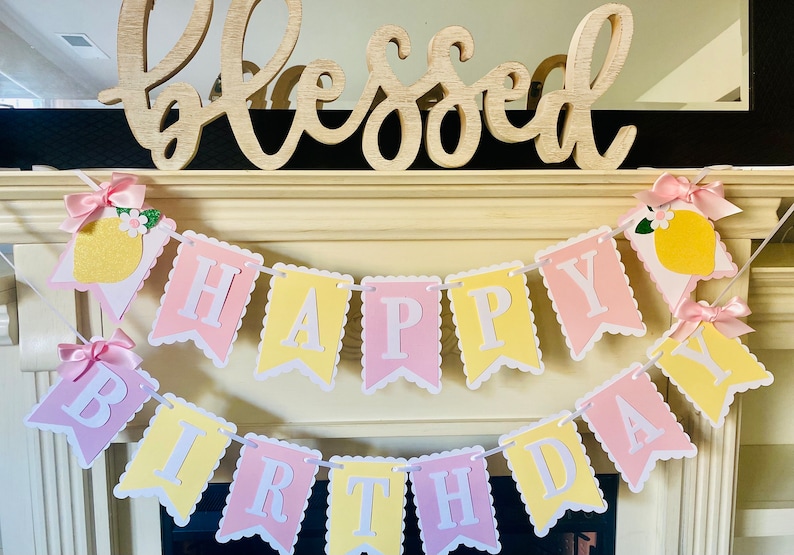 May include: A yellow and pink banner with the words "Happy Birthday" in white letters. The banner is decorated with lemons and flowers.