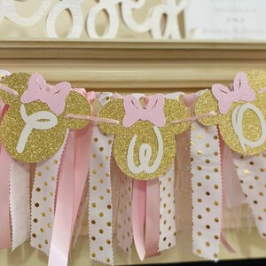 May include: A festive banner with gold glitter Mickey Mouse head shapes, each with a pink bow and a white letter spelling "One". The banner is adorned with pink and white polka dot ribbons, perfect for a birthday celebration.