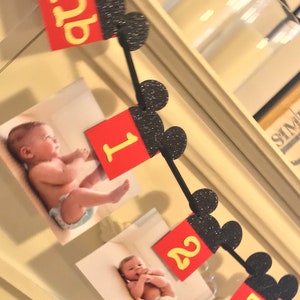 May include: A black and red Mickey Mouse themed banner with pictures of a baby and the numbers 1, 2, and 3. The banner is made of felt and has glitter on the Mickey Mouse ears.