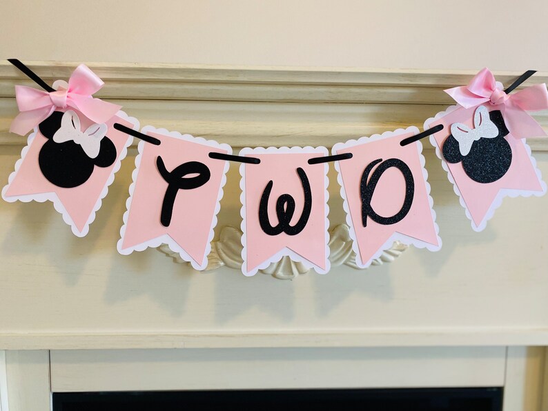May include: Pink and black banner with the word "TWO" in black script letters. The banner is decorated with two black and white Minnie Mouse heads with pink bows.
