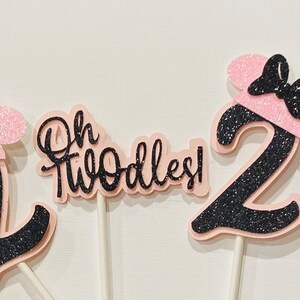 May include: Three pink and black glitter cake toppers with the number 2 and the text "Oh Twodles!"