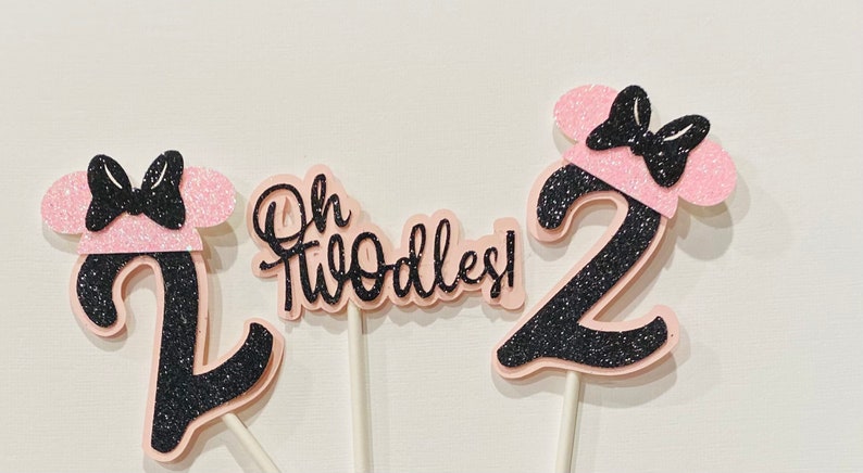 May include: Three pink and black glitter cake toppers with the number 2 and the text "Oh Twodles!"