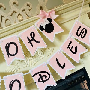 May include: Pink and black banner with the words "Oh Boy" and a Disney Mickey Mouse head with a pink bow. The banner is strung together with white string.