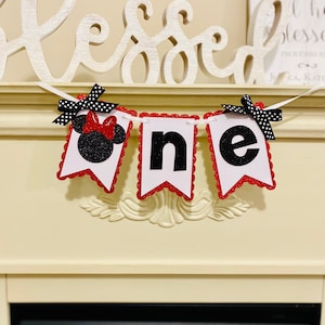 May include: A decorative banner featuring three white pennants with scalloped red glitter edges. The first pennant displays a black glitter mouse silhouette with a red bow, while the others show the black letters n and e. Black and white polka dot bows are attached to the top corners.