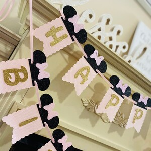 May include: Pink and black banner with gold glitter letters spelling "Happy Birthday". Each letter is attached to a black Mickey Mouse ear with a pink bow.