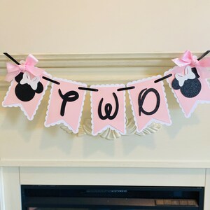 May include: Pink and black banner with the word "TWO" in black letters and two black and white Minnie Mouse heads on either end.