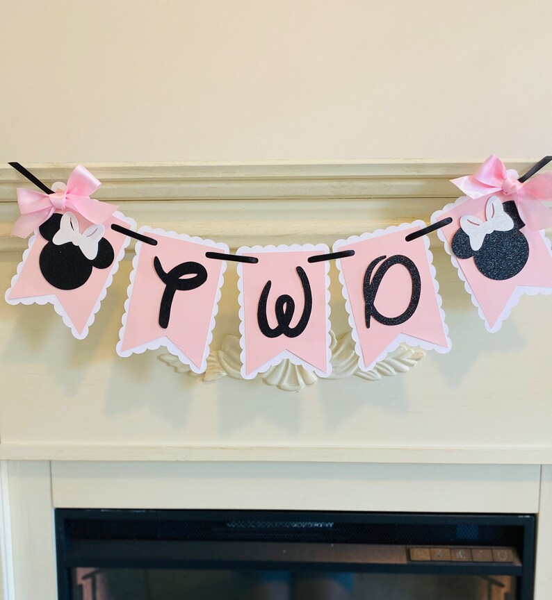 May include: Pink and black banner with the word "TWO" in black letters and two black and white Minnie Mouse heads on either end.