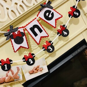 May include: A red and black Minnie Mouse themed banner with the word "one" and numbers 1 through 6. The banner is strung with white string and has red bows with black polka dots. There are photos of a baby in the bottom of the image.