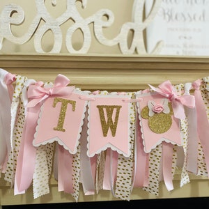 May include: A pink and gold banner with the letters "TW" and a Minnie Mouse silhouette. The banner is decorated with pink ribbons, white fabric with gold polka dots, and pink bows. The word "Blessed" is visible in the background.