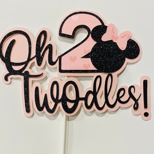 May include: Pink and black cake topper with the text "Oh Two-dles!" and a number 2 with pink hearts. A black silhouette of a mouse head with a pink bow is next to the number 2.