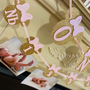 May include: Gold and pink glitter Minnie Mouse themed banner with photos and the numbers 1, 2, 3, 4, and the word "One".