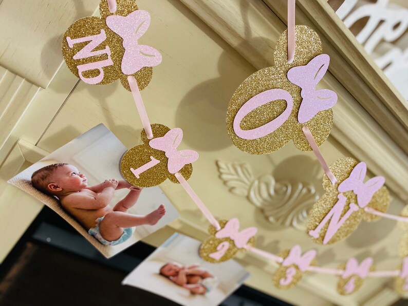 May include: Gold and pink glitter Minnie Mouse themed banner with photos and the numbers 1, 2, 3, 4, and the word "One".