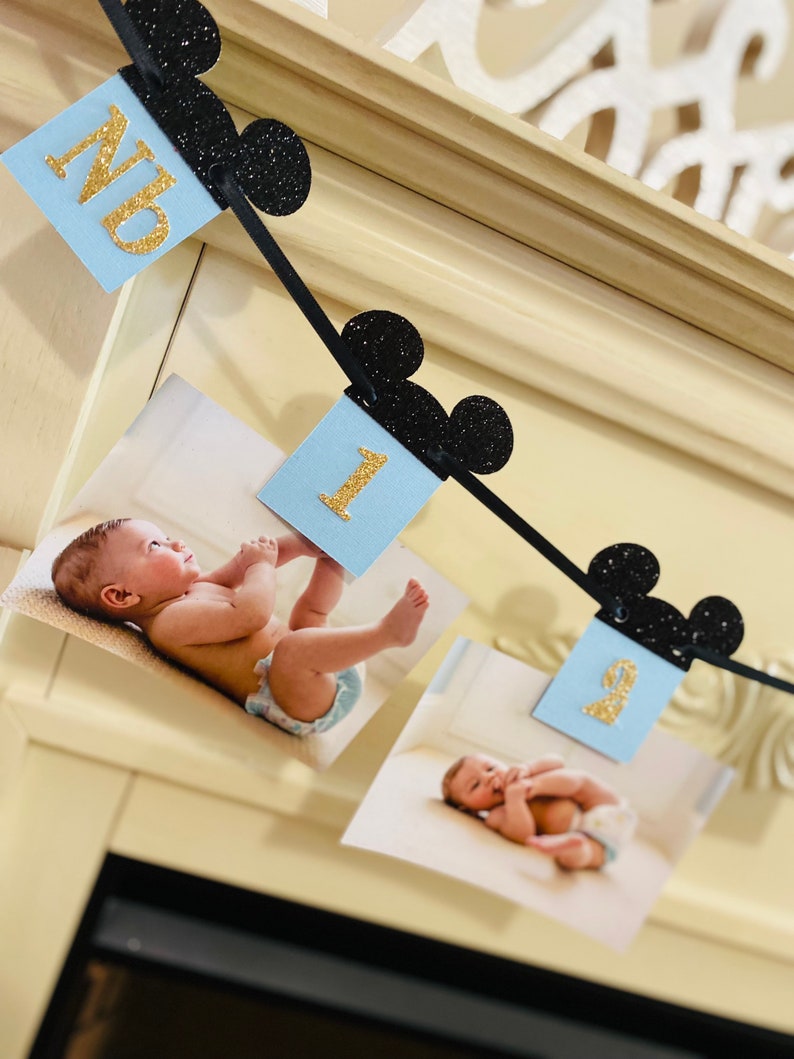 Pode incluir: Uma faixa tem&aacute;tica do Mickey Mouse em preto e dourado com cart&otilde;es azuis e brancos com os n&uacute;meros 1 e 9. A faixa &eacute; decorada com orelhas do Mickey Mouse pretas com glitter.