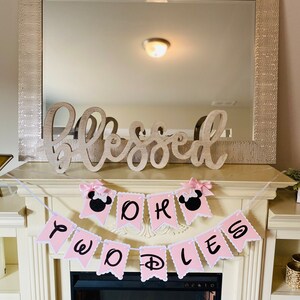 May include: Pink and white banner with the words "Oh Two D's" and black Mickey Mouse ears on each end. The banner is hanging above a fireplace.