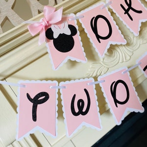 May include: Pink and black banner with the words "Two" and a black silhouette of Minnie Mouse with a pink bow.