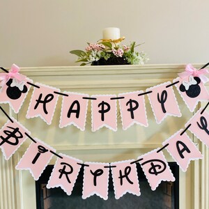 Puede incluir: Bandera de feliz cumplea&ntilde;os rosa y negra con personajes de Minnie Mouse en cada extremo. La bandera est&aacute; hecha de cartulina y tiene un borde festoneado.