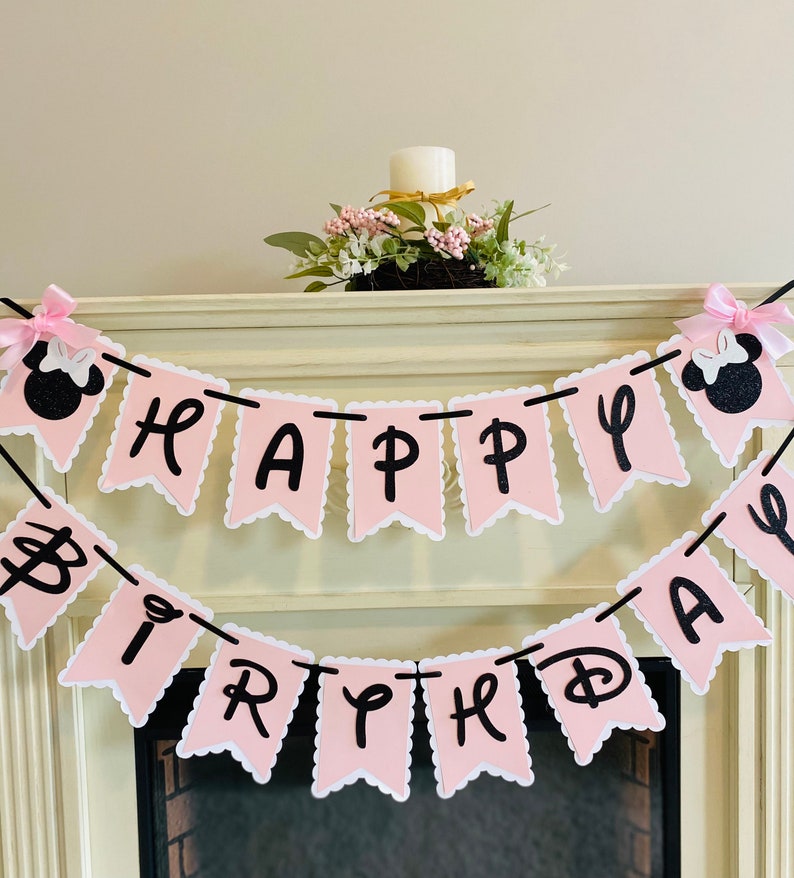 Puede incluir: Bandera de feliz cumplea&ntilde;os rosa y negra con personajes de Minnie Mouse en cada extremo. La bandera est&aacute; hecha de cartulina y tiene un borde festoneado.