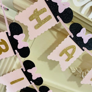 May include: Pink and black banner with gold glitter letters spelling "Happy Birthday". Each letter is on a separate flag with a black Mickey Mouse ear and pink bow.